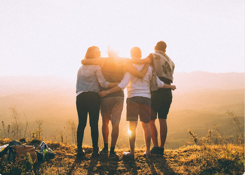 fellowship about Group of people standing arm in arm looking onto a sunset on a mountain.