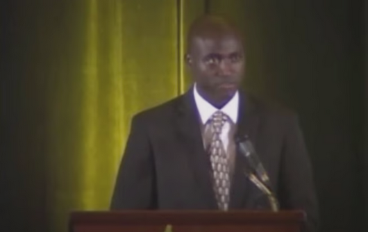 Omar Bah on a podium making a speech on refugee voices.